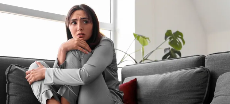 Młoda kobieta czuje lęk, skulona na sofie, jej wzrok pełen obawy