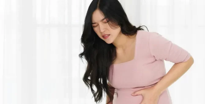 Młoda Azjatka odczuwająca silne dolegliwości bólowe trzyma się za brzuch