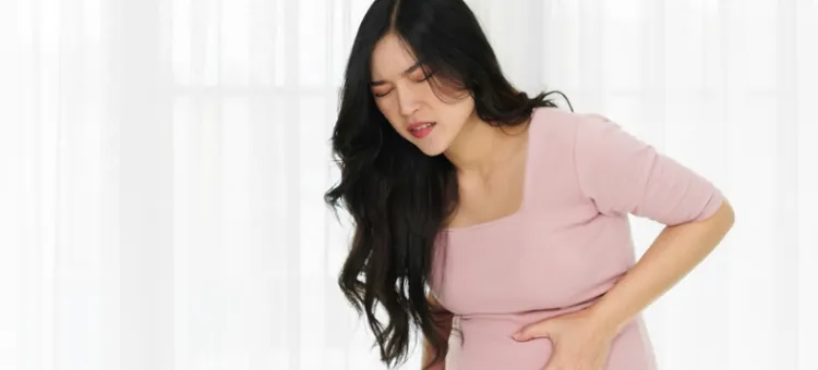 Młoda Azjatka odczuwająca silne dolegliwości bólowe trzyma się za brzuch