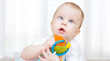 Zaciekawione niemowlę z zezem trzyma w rączkach barwną zabawkę