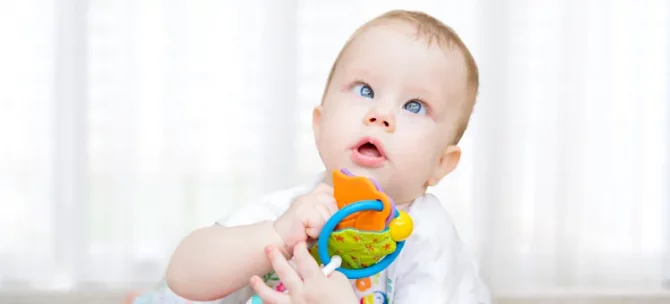 Zaciekawione niemowlę z zezem trzyma w rączkach barwną zabawkę