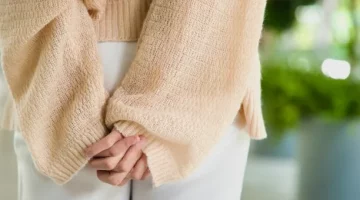 Dłonie dyskretnie ułożone na pośladkach kobiety w białych spodniach i w delikatnym beżowym swetrze