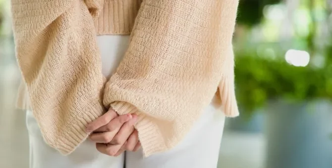 Dłonie dyskretnie ułożone na pośladkach kobiety w białych spodniach i w delikatnym beżowym swetrze