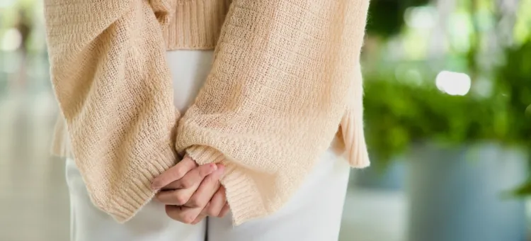 Dłonie dyskretnie ułożone na pośladkach kobiety w białych spodniach i w delikatnym beżowym swetrze