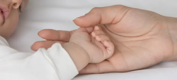 Czułe połączenie dorosłej ręki obejmującej maleńką dłoń niemowlęcia w geście opieki na białej pościeli