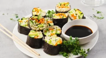 Aromatyczne rolki sushi z ogórka, marchewki i awokado starannie przygotowywane na talerzu obok sosu