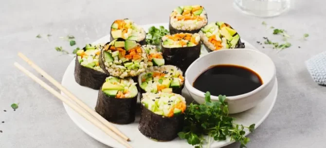 Aromatyczne rolki sushi z ogórka, marchewki i awokado starannie przygotowywane na talerzu obok sosu
