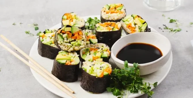 Aromatyczne rolki sushi z ogórka, marchewki i awokado starannie przygotowywane na talerzu obok sosu