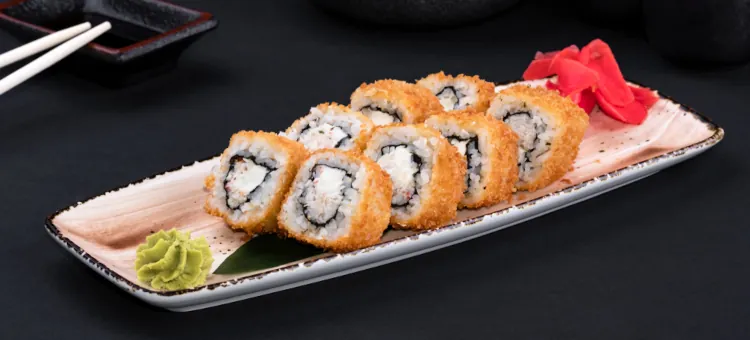 Złociste kawałki japońskiego sushi w chrupiącej panierce podane z dodatkami wasabi i marynowanego imbiru na talerzu na czarnym tle