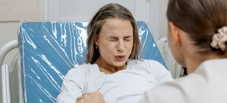 Zmęczona trudami porodu pacjentka na łóżku, w obecności troskliwego personelu medycznego