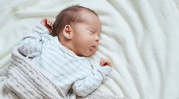 Dziecko w wieku niemowlęcym błogo śpi, otulone miękkim jasnym pledem