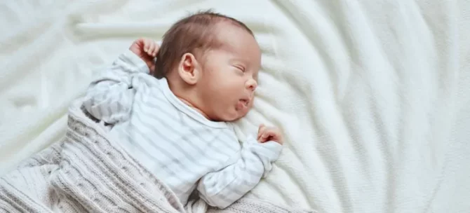 Dziecko w wieku niemowlęcym błogo śpi, otulone miękkim jasnym pledem