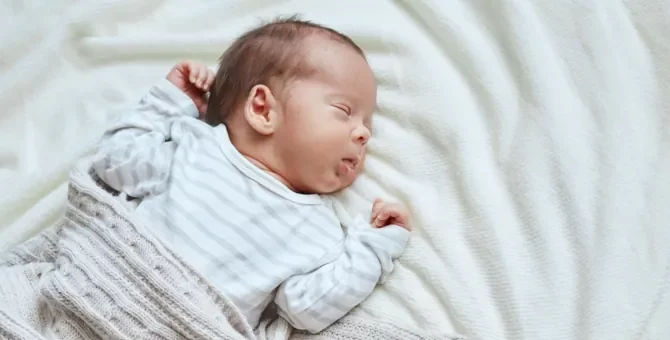 Dziecko w wieku niemowlęcym błogo śpi, otulone miękkim jasnym pledem