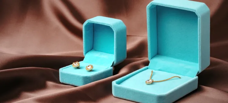 Złoty naszyjnik i kolczyki w lazurowych opakowaniach na brązowym suknie, gotowe na prezent