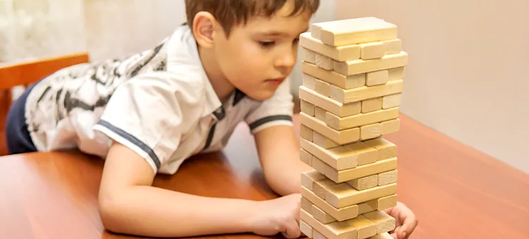 Chłopiec skupiony podczas budowania wieży z drewnianych klocków