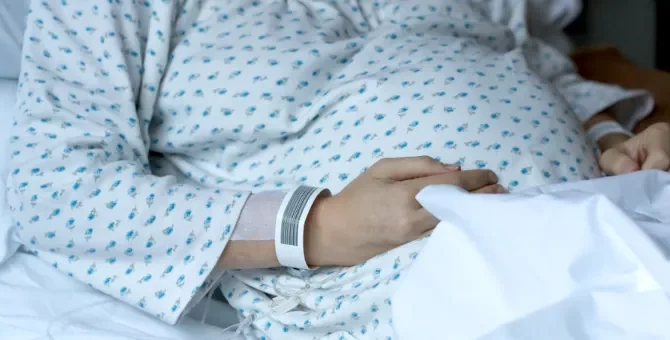 Pacjentka w jasnej piżamie na szpitalnym łóżku wyczekuje przyjścia na świat swojego maleństwa