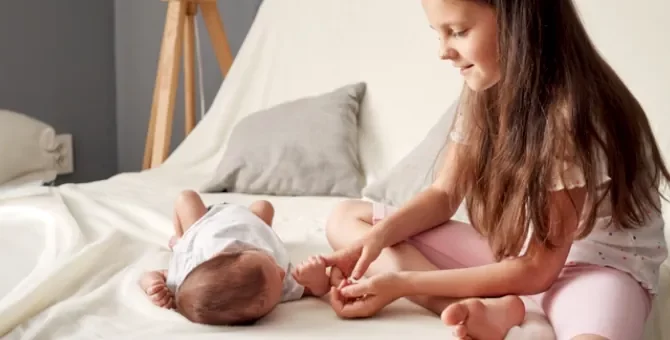 Mała siostra podaje palec noworodkowi na jasnej pościeli łóżka