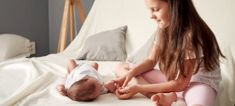 Mała siostra podaje palec noworodkowi na jasnej pościeli łóżka