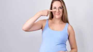 Ciężarna, uśmiechnięta pani w okularach na nosie, pokazuje swój nos