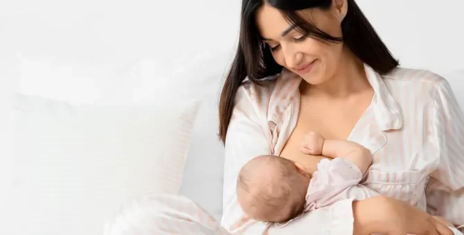 Młoda matka na jasnym tle z czułością zapewnia pokarm swojemu nowo narodzonemu dziecku, karmiąc piersią