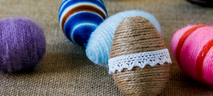 Różnokolorowe ozdoby świąteczne z włóczki i sznurka na jajkach, położone na beżowej tkaninie