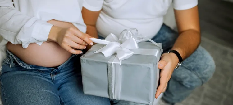 Przyszła mama w ciąży rozwiązuje wstążkę na eleganckim upominku w towarzystwie przyszłego taty, zbliżenie na zawinięty prezent