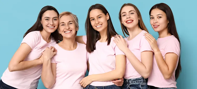 Radosne panie w różowych koszulkach, pokazujące wzajemną przyjaźń oraz siłę, na jasnoniebieskim tle