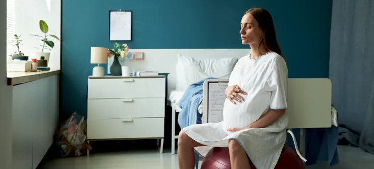 Przyszła matka koncentruje się na opanowaniu skurczów, głęboko oddychając w pozycji siedzącej na piłce, w pomieszczeniu o spokojnym błękitnym tle