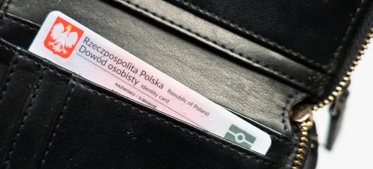 Elegancka czarna portmonetka z wystającym z niej polskim dokumentem tożsamości na jasnym tle
