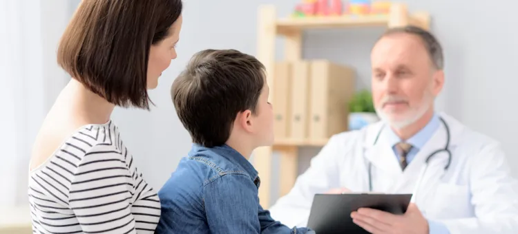 Mężczyzna w białym fartuchu udziela porady małemu pacjentowi z opiekunką na jasnym tle