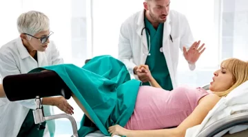 Kobieta w trakcie akcji porodowej otrzymuje wsparcie wykwalifikowanego personelu medycznego na jasnym tle sali szpitalnej
