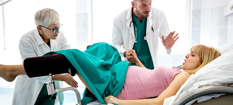 Kobieta w trakcie akcji porodowej otrzymuje wsparcie wykwalifikowanego personelu medycznego na jasnym tle sali szpitalnej