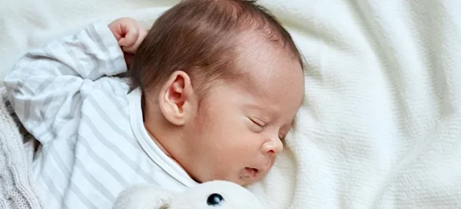 Niemowlę spokojnie odpoczywa na jasnym, miękkim posłaniu