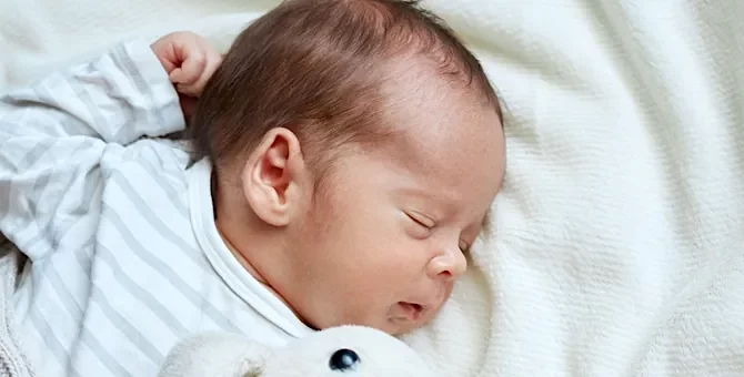 Niemowlę spokojnie odpoczywa na jasnym, miękkim posłaniu