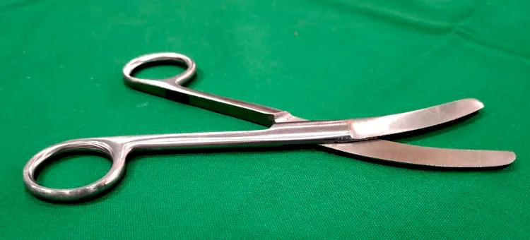 Metalowe nożyczki do nacinania krocza, o zakrzywionych ostrzach, spoczywają na zielonej powierzchni medycznej