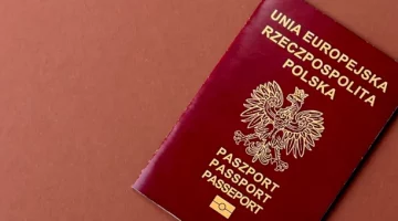 Bordowy paszport ze znakiem orła, na terakotowym tle, potwierdzający obywatelstwo polskie