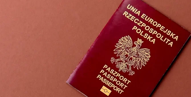 Bordowy paszport ze znakiem orła, na terakotowym tle, potwierdzający obywatelstwo polskie