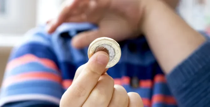 Dłoń dziecka delikatnie obejmująca błyszczącą monetę na rozmytej jasnej płaszczyźnie
