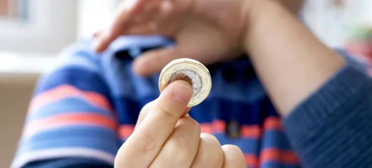 Dłoń dziecka delikatnie obejmująca błyszczącą monetę na rozmytej jasnej płaszczyźnie