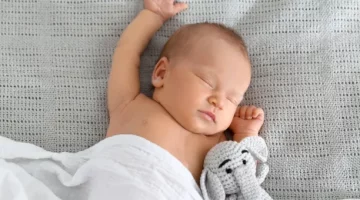 Spokojna drzemka niemowlęcia z pluszowym słonikiem na jasnym tle