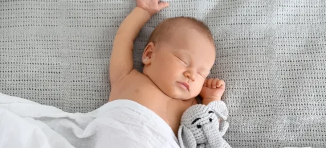 Spokojna drzemka niemowlęcia z pluszowym słonikiem na jasnym tle