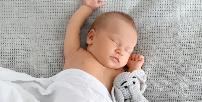 Spokojna drzemka niemowlęcia z pluszowym słonikiem na jasnym tle