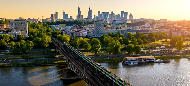 Składy kolejowe przemierzające konstrukcję mostu nad Wisłą na tle złocistego późnego popołudnia