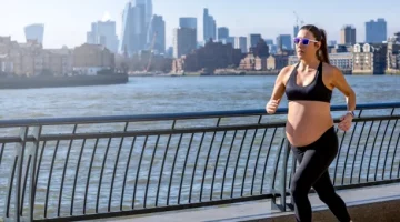 Aktywnie ćwicząca przyszła mama pokonuje trasę po jasnej betonowej nawierzchni, z rzeką o granatowej wodzie i miejskim pejzażem w słonecznym tle