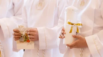Chłopcy w białych szatach ze świecami podczas Pierwszej Komunii Świętej, na jasnym tle, zbliżenie na ręce