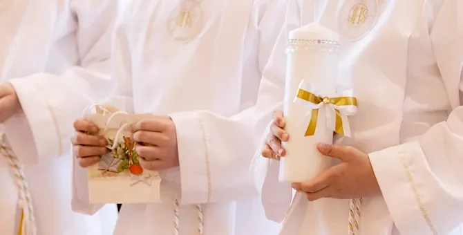 Chłopcy w białych szatach ze świecami podczas Pierwszej Komunii Świętej, na jasnym tle, zbliżenie na ręce