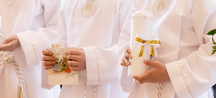Chłopcy w białych szatach ze świecami podczas Pierwszej Komunii Świętej, na jasnym tle, zbliżenie na ręce