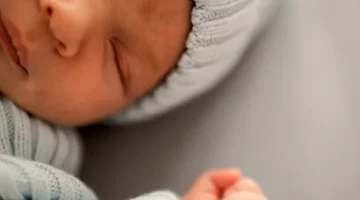 Malutkie niemowlę drzemie w jasnoszarym otulaczu na jasnym, neutralnym tle