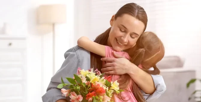Rodzinne objęcie matki i dziewczynki, pełne ciepła i różnokolorowych kwiatów, na jasnym domowym tle