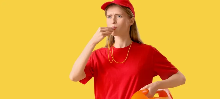 Dziewczyna-ratownik w czerwonym t-shircie i daszku daje głośny sygnał na jednolitym żółtym tle, trzymając pomarańczową boję